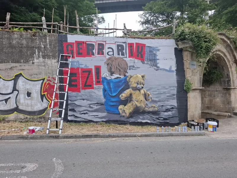 Mural con la leyenda Gerra rik ez, un niño de azul y un oso de peluche